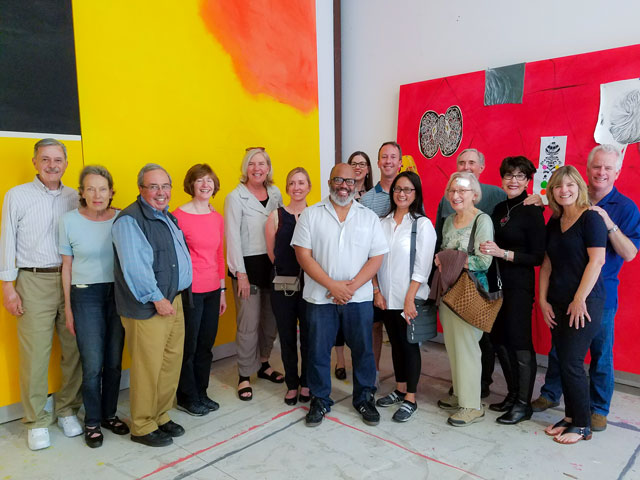 A group of people poses in front of colorful artwork in a gallery or studio space.