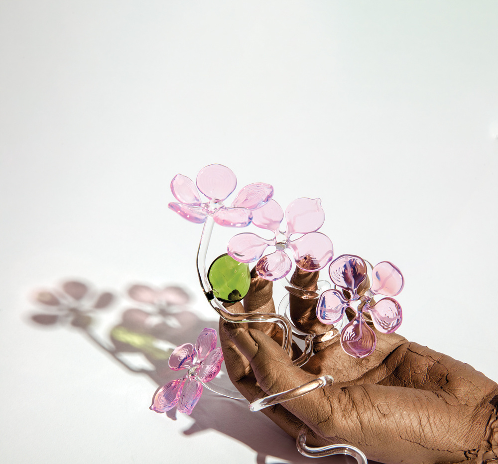 A bronze hand sculpture holds delicate pink glass flowers with a green leaf.