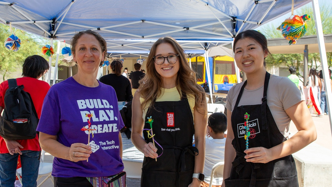 three staff members from different organizations each holding up a stick with miniature clay art