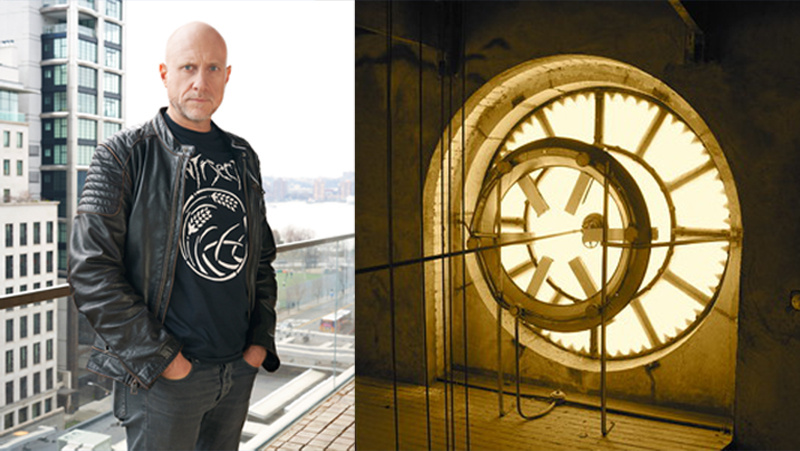 Man with shaved hair wearing black and an internal shot of a clock.