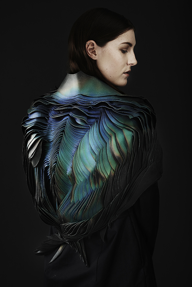 A woman carefully turning to the viewer. Upon closer examination of her clothing, large Iridescent feathers fold in upon themselves into/onto her back.  
