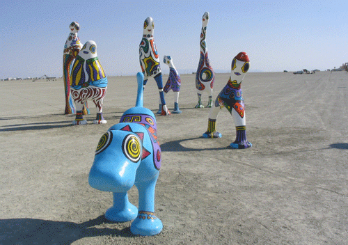 In the desert: colorful anthropomorphized statues that are posed as though in motion towards the viewer. They are painted with random shapes and spots and their bodies do not match any animal or human.