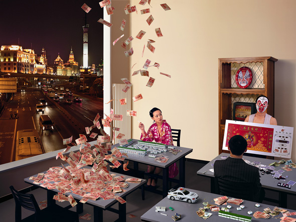 At night, a bright sparse room with cards flying up or falling down. A woman is playing a game with tiles. A man plays cards while a man wearing a wrestling mask holds a poster for him. Behind them is a table with cash, playing cards, and a toy police car. The cityscape is lit up.