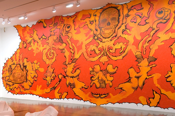 A bright orange and red graphic depicting fire and heat. It is a mirrored image that centers at a skull. The eyes are removed from the skull and float in the background. There are squiggly lines look like brain tissue floating throughout the work.