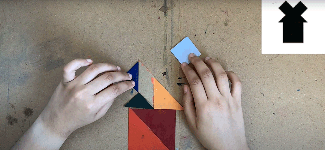 Video still of a person arrangeing pieces of paper cut in geometric shapes.