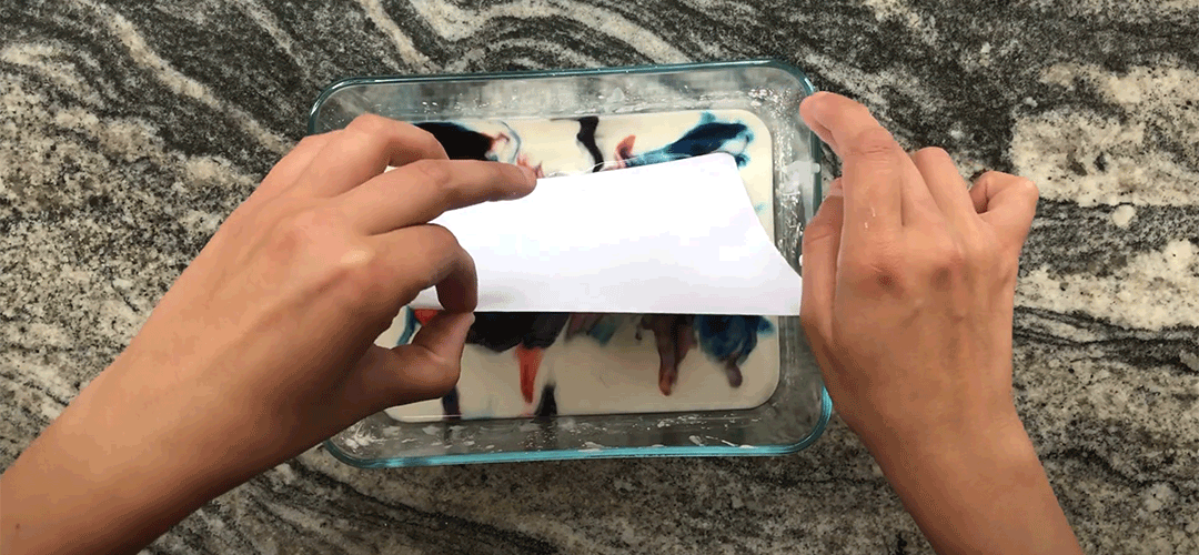 Video still of a person pressing a sheet of white paper on a plate with color inks.
