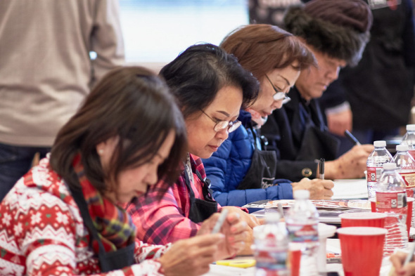 Four older Asian adults look down at art they are individually creating while sitting close to each other at a table.