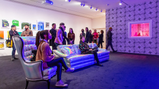 Visitors in a living room-inspired gallery, sitting on holographic couches.