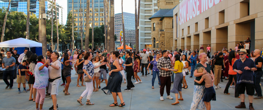 Dancers in an outdoor plaza with palm trees.