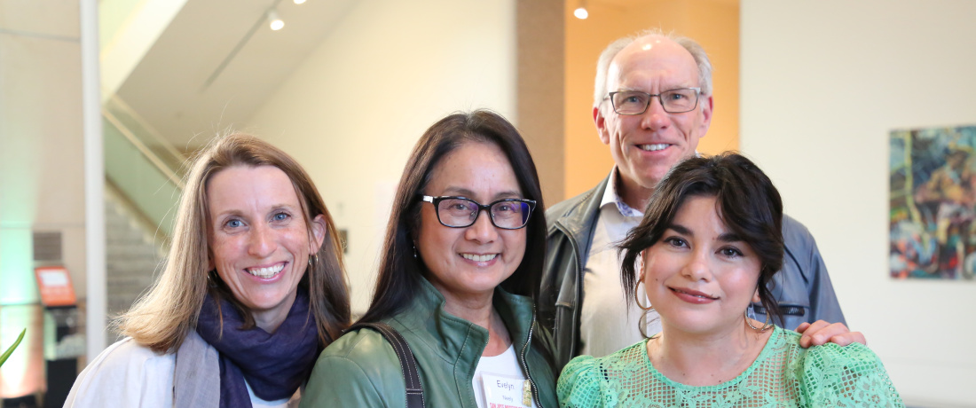 Four smiling people pose at an indoor event at the San José Museum of Art, with name tags and artwork in the background.