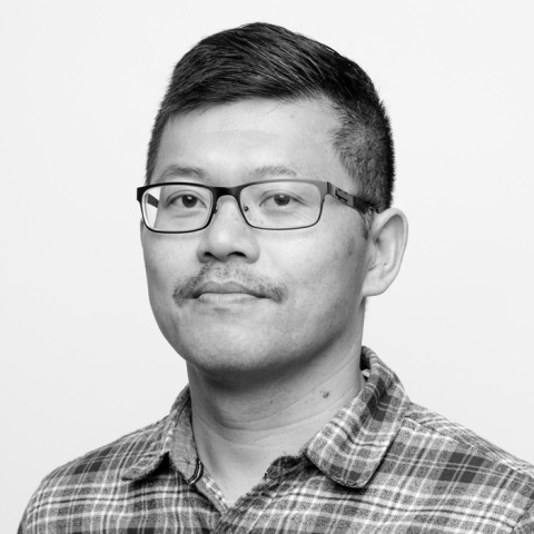 Black-and-white headshot of a man wearing glasses and a plaid shirt.