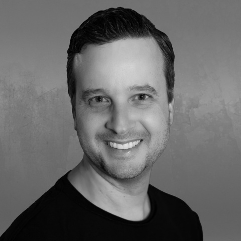 Black-and-white headshot of a man smiling against a textured gray background.