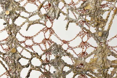 A delicate copper material is weaved into thin chains. These connect to another thicker material that simultaneously looks like sea coral and rope.