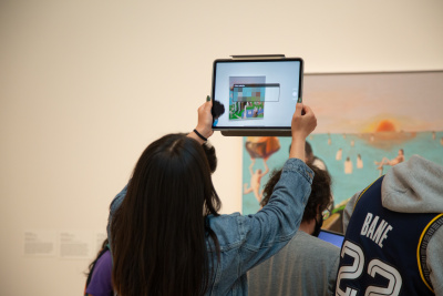 a visitor holding up a tablet in front of an artwork