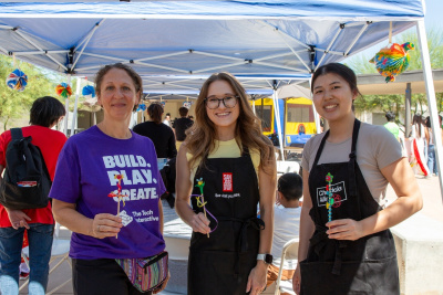 three staff members from different organizations holding up a stick with miniature clay art