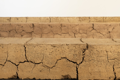 Three sharply angled steps are made of what looks like cracking adobe. Bits of straw can be seen sticking out. 