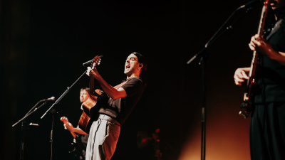 man enthusiastically singing on stage with two band members on guitars