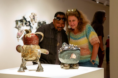 a couple amused with ceramic sculptures of imaginative creatures on a pedestal