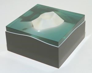 Acrylic cube with a grey base covered by turquoise translucent water. A white island shaped like a volcano emerges from the middle of the sea.