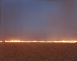 A photograph of a thin horizontal line of fire that separates the smoky blue sky and a desert field.