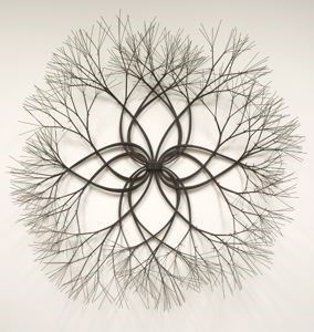 A sculpture combined of small branches woven together, formed to look like a blooming flower. Thicker stems are in the middle and then thinner multiple branches open up at the end of each stem, shooting outwards in every direction, creating a delicate circle.