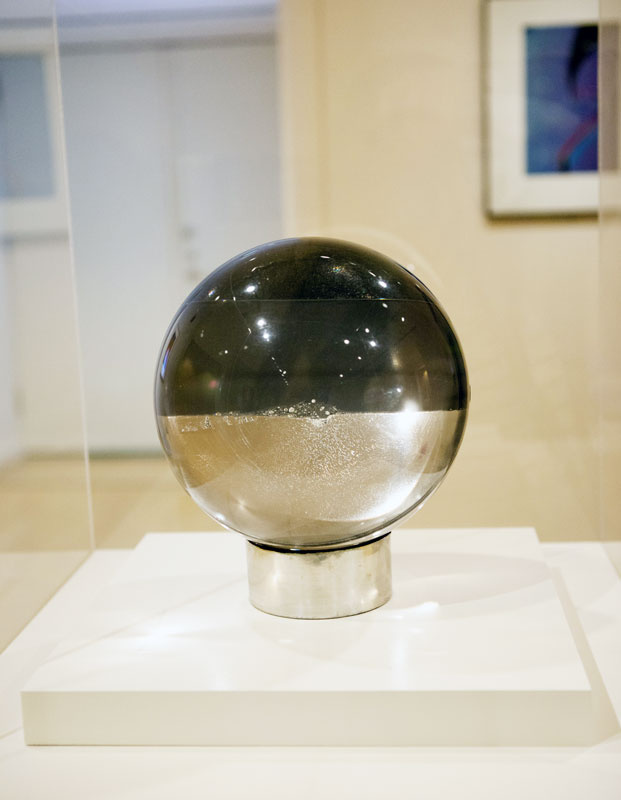 A sphere containing acrylic resin and mercury on a lead base. Half of the sphere is grey and the other half is gold. The sphere reflects its surrounding lighting. 