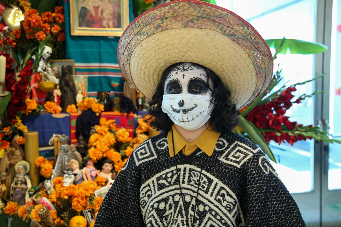 Person wearing skull makeup, a poncho, and a straw hat in front of an altar.