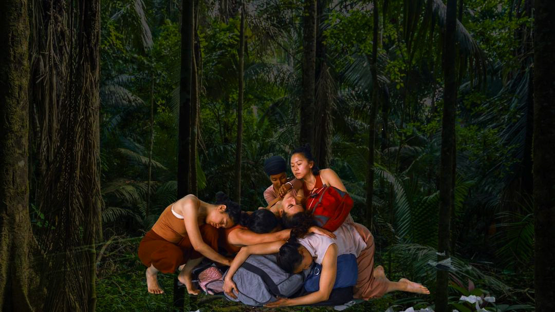 Six women of color entangled in a formation in a rainforest.