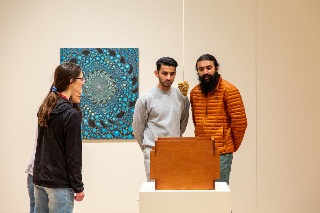 People intently looking at a frozen pyramid of pebbles melting in a gallery.