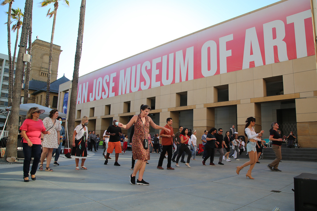 Dancers in an outdoor plaza with palm trees.