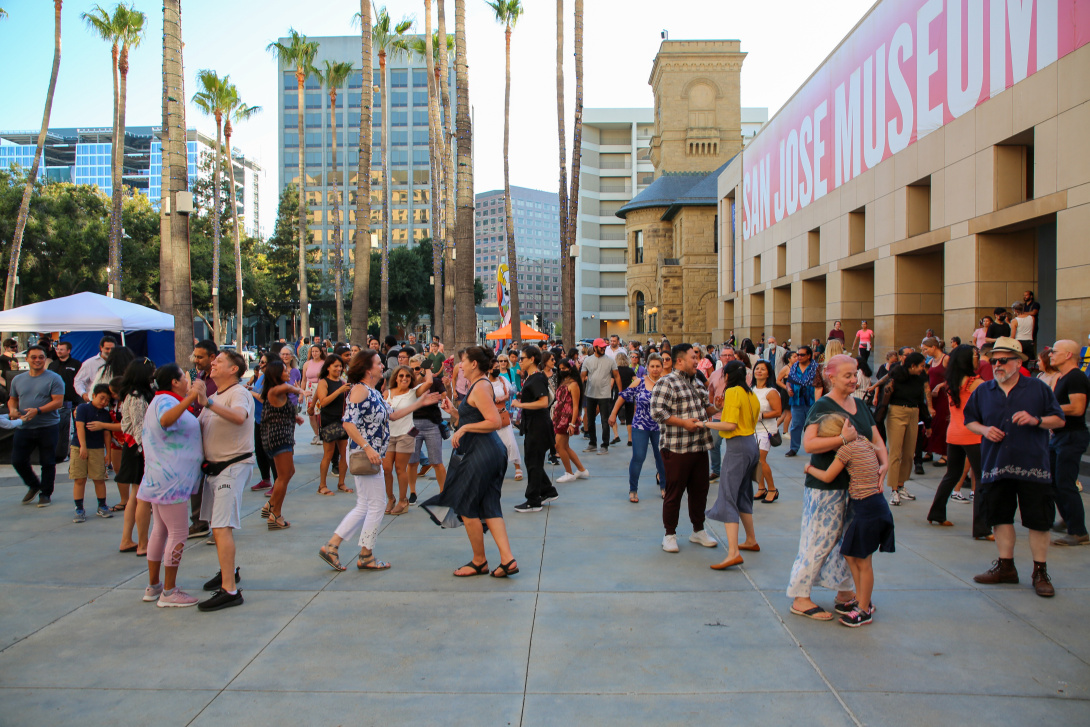 Dancers in an outdoor plaza with palm trees.