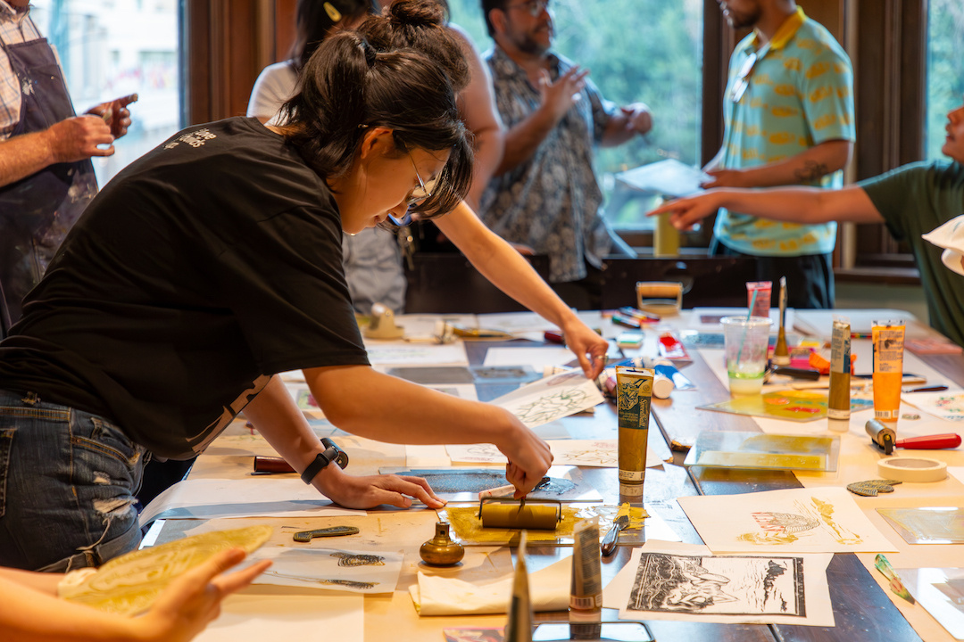 a student wearing a black t-shirt rolling ink to make a relief print in a classroom setting