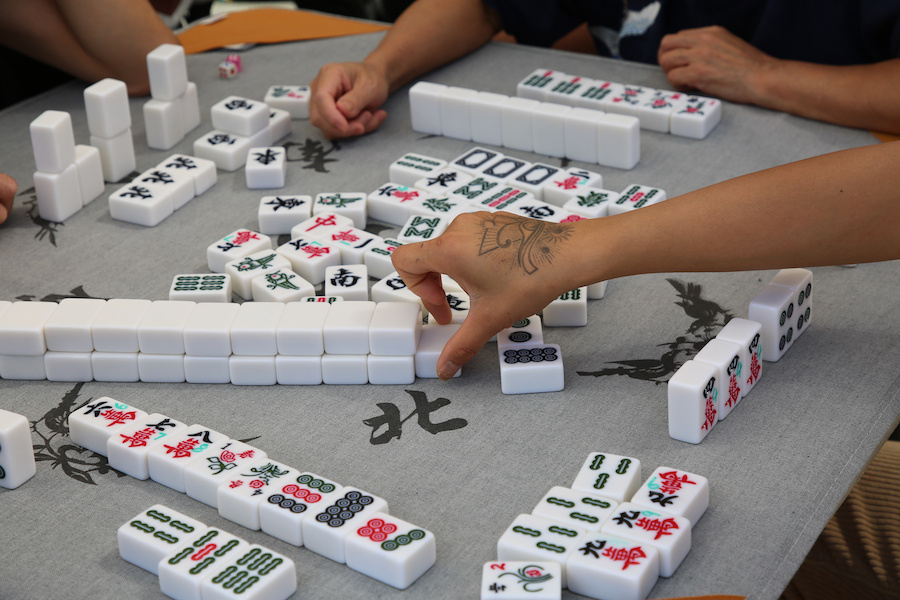 closeup photograph of a mahjong table with hands grabbing tiles