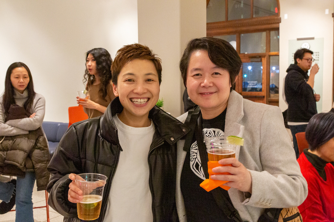Two East Asian women with short hair holding up their glasses of beer