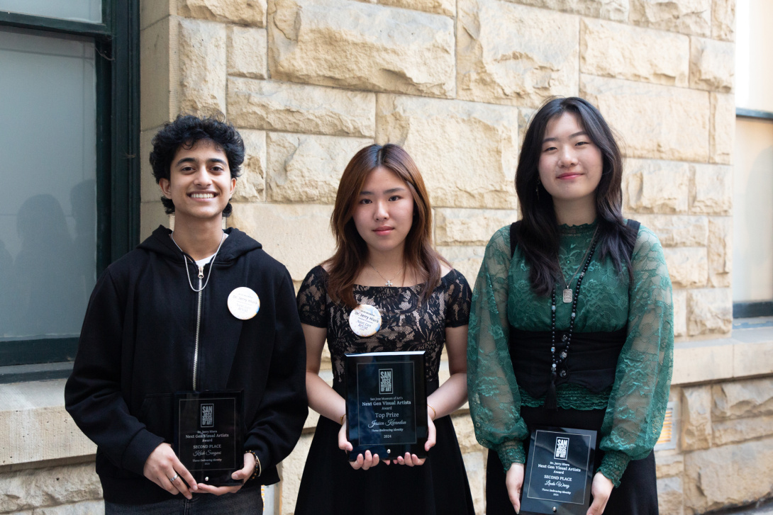 Three young teens face the camera, holding award plaques—one male and two females. The male and one of the females smile broadly.