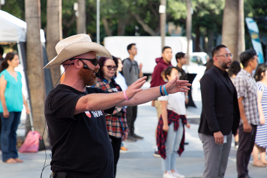 man wearing a western hat with arms out and instructing a crowd