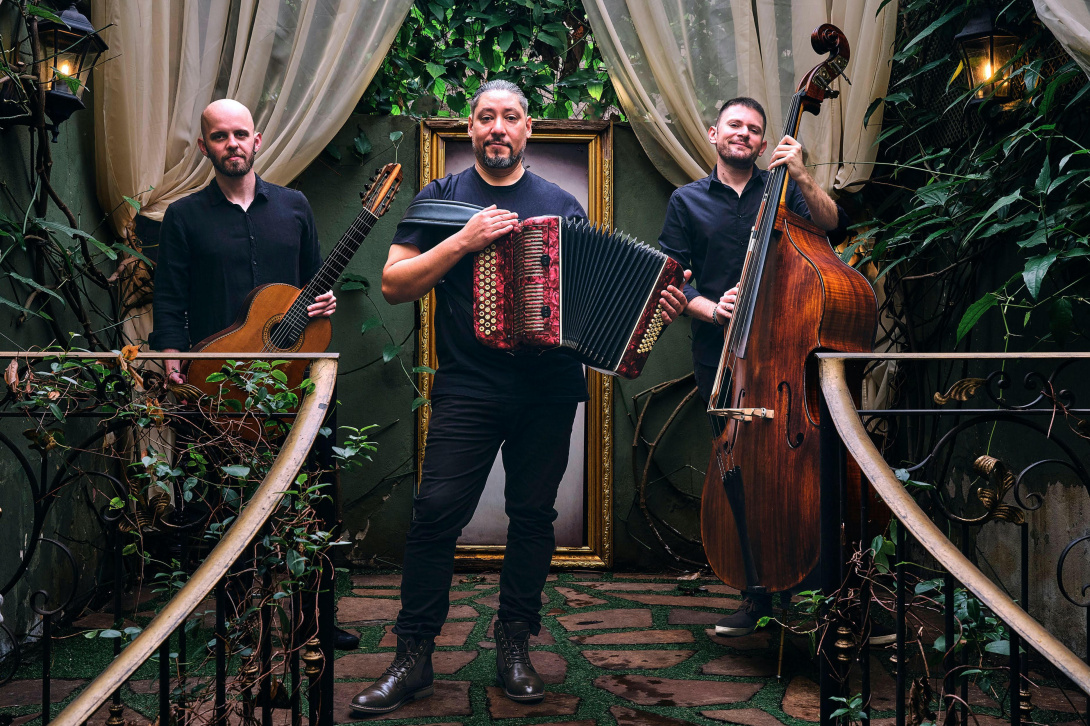 Three musicians on a lush stage carrying instruments