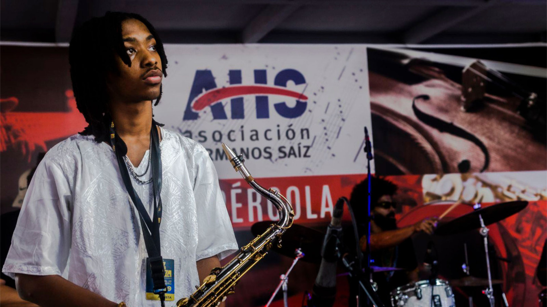 young Black man with medium length dreads on stage with a saxophone