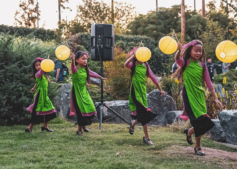 four young girls skipping with illuminated lanterns wearing traditional Vietnamese dresses ao dai dresses