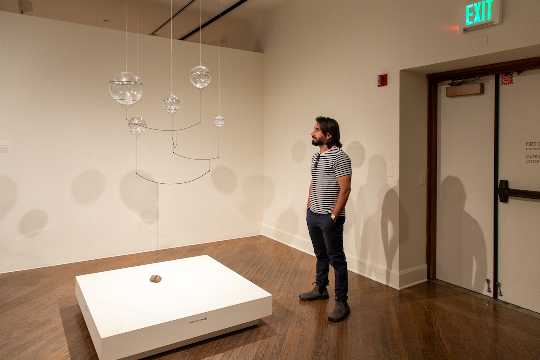 man looking up towards an upside down mobile of glass spheres