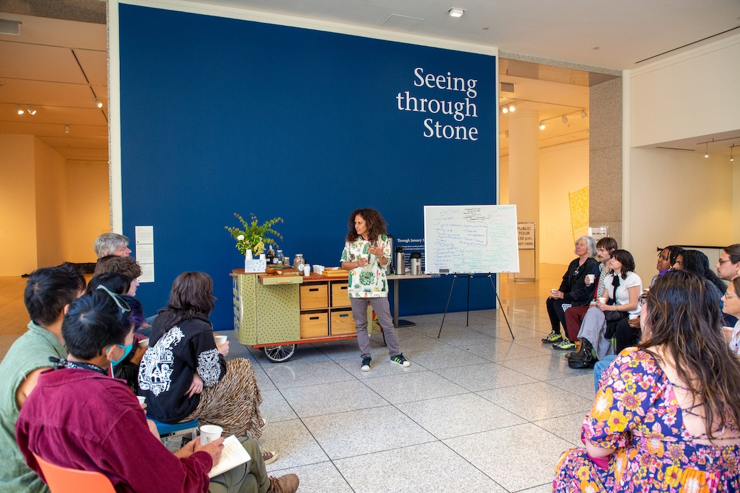 woman leads a discussion with a cart of herbs and dried plants behind her