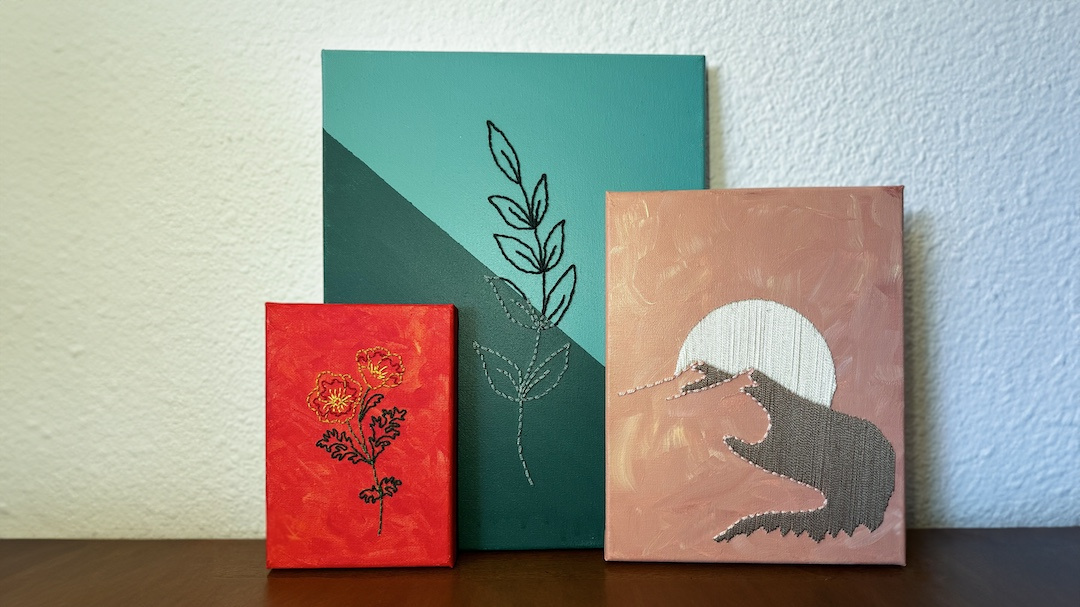 three painted canvases with embroidered imagery of flowers, leaves and a mountain