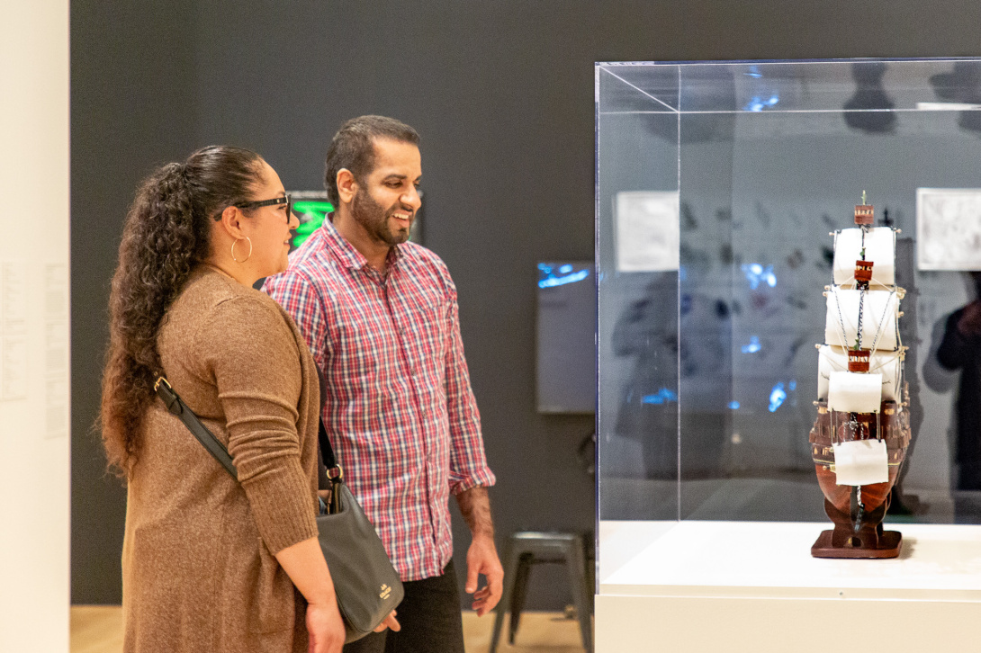 two visitors looking at a replica of a ship in an enclosed vitrine