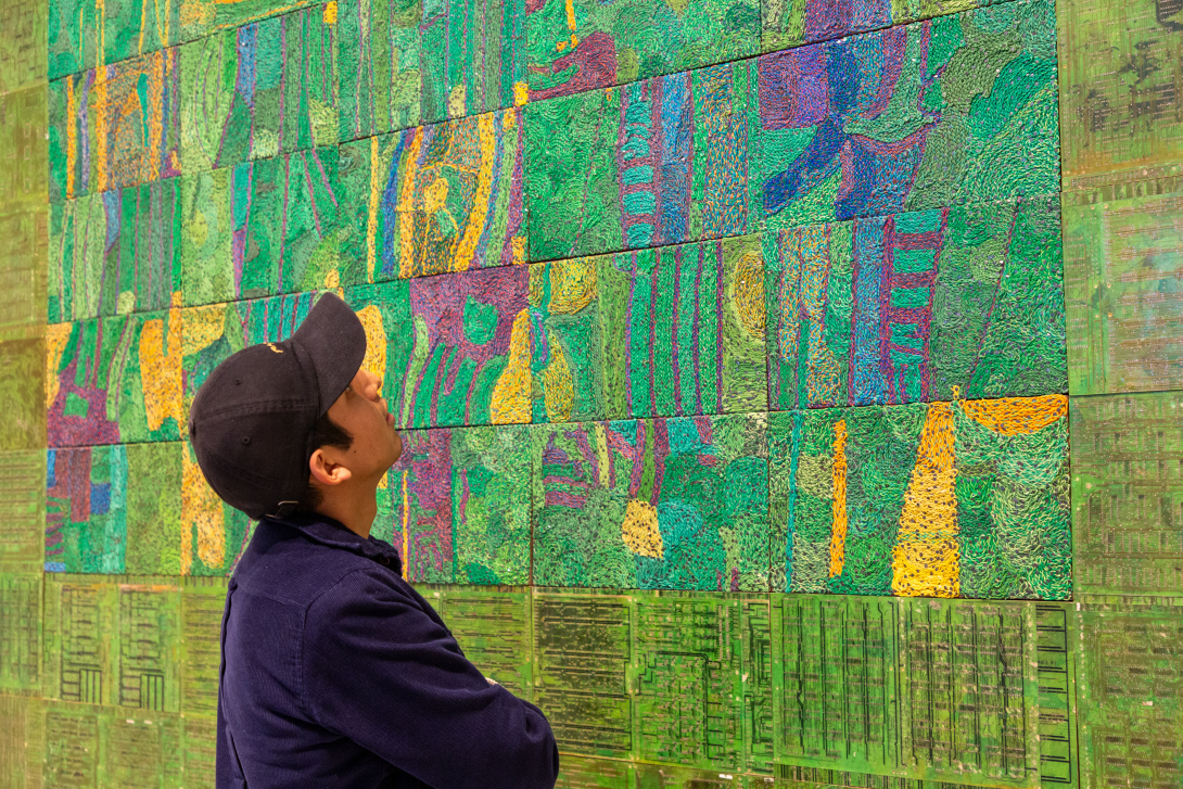 Visitor observing a large, colorful wall artwork made from recycled materials in Elias Sime’s Tightrope exhibition at SJMA.