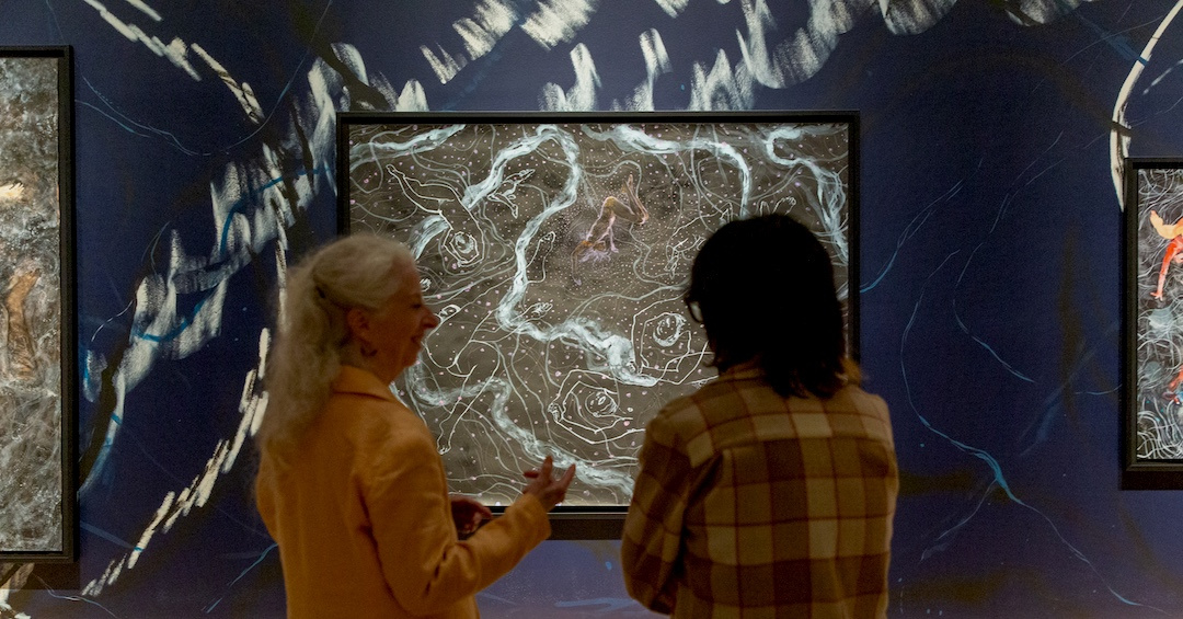 two women conversing in front a painting depicting ghostly Black bodies in space