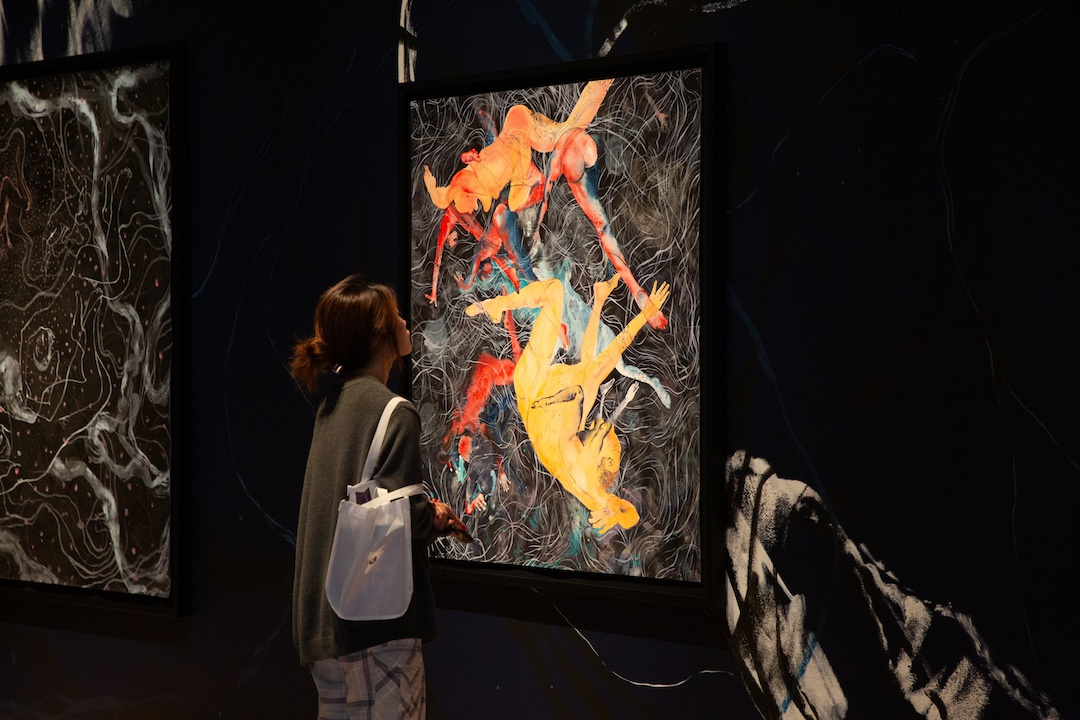 woman looking at a figurative painting with colorful bodies floating in space