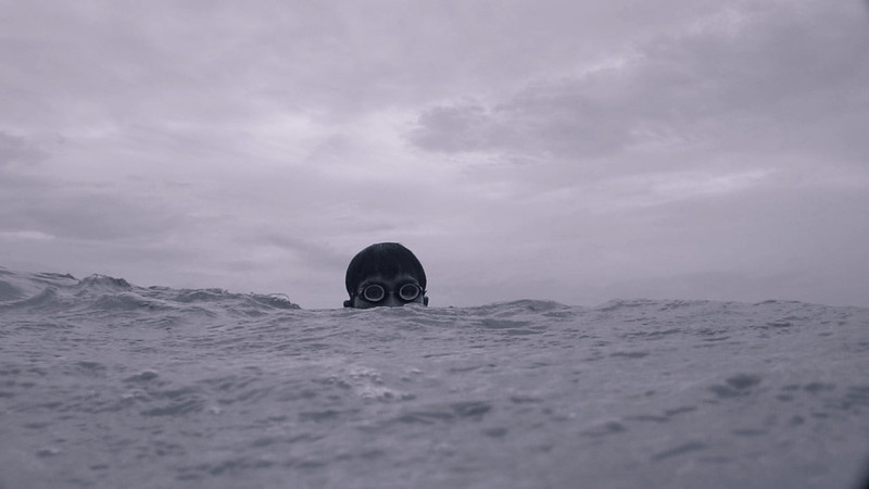 a video still of a young Filipino person peeking his head out of the sea wearing goggles