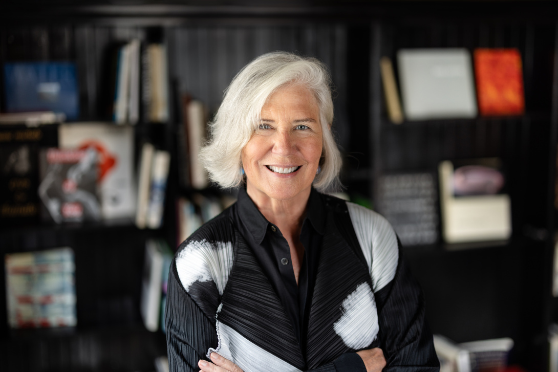 a smiling white woman with white and gray hair in a bob in front of a bookshelf