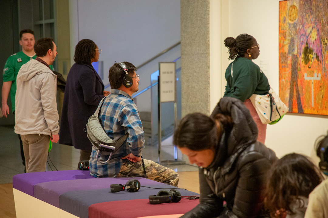 visitors in a gallery listening to sound art and looking at a painting