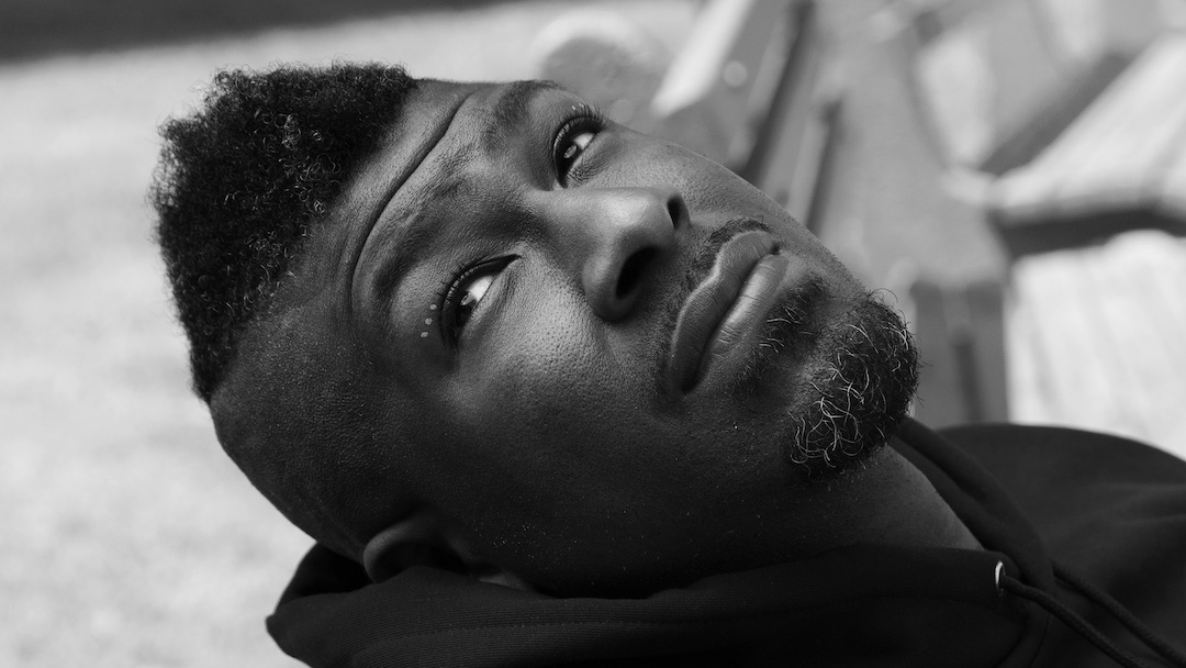 black man with a mohawk leaning back on a park bench gazing up